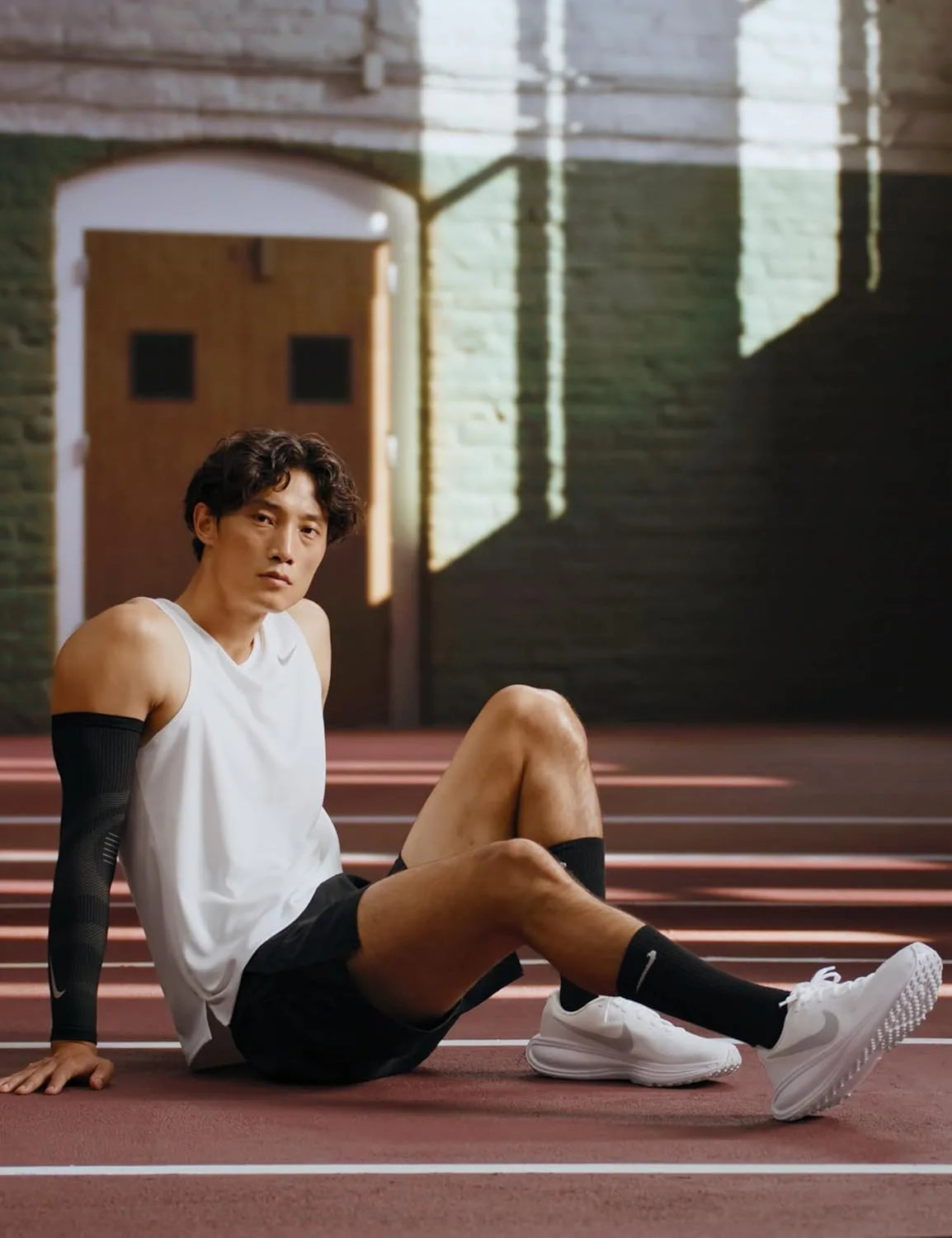 A runner in white Nike Revolution 8 running shoes sitting on an indoor track after a workout