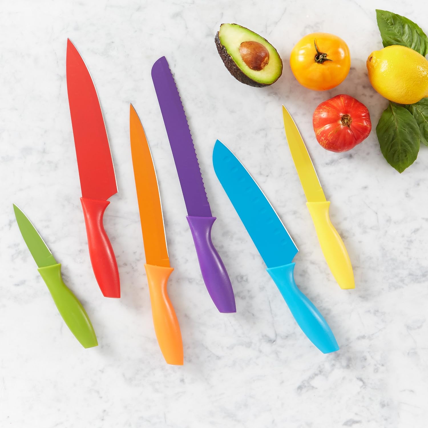 Amazon Basics color-coded kitchen knives laid out on a marble counter next to fresh tomatoes, an avocado, and basil