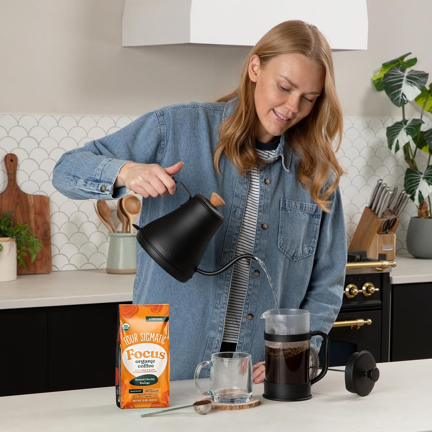 A person pouring hot water into a pour-over brewer next to a bag of Four Sigmatic Focus mushroom ground coffee in a kitchen