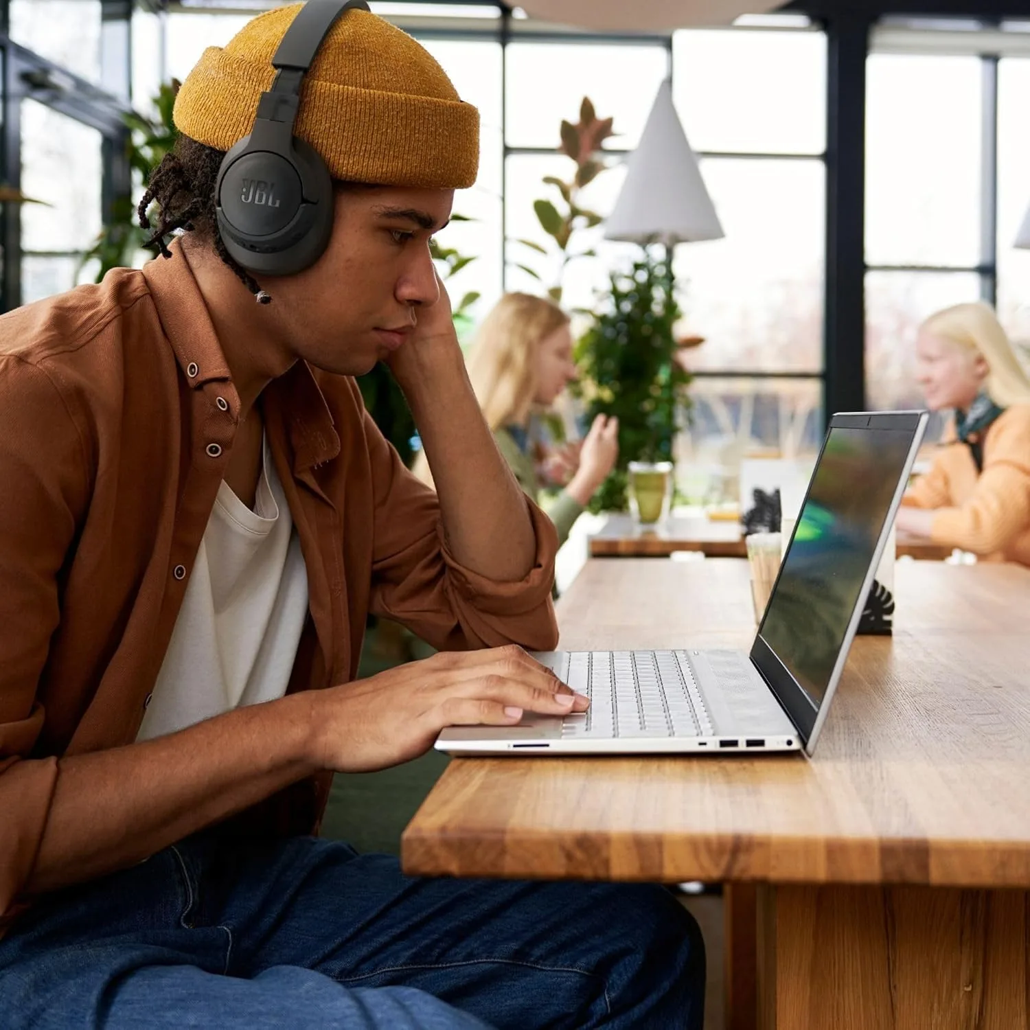 Man wearing black over-ear headphones while working on a laptop in a cafe