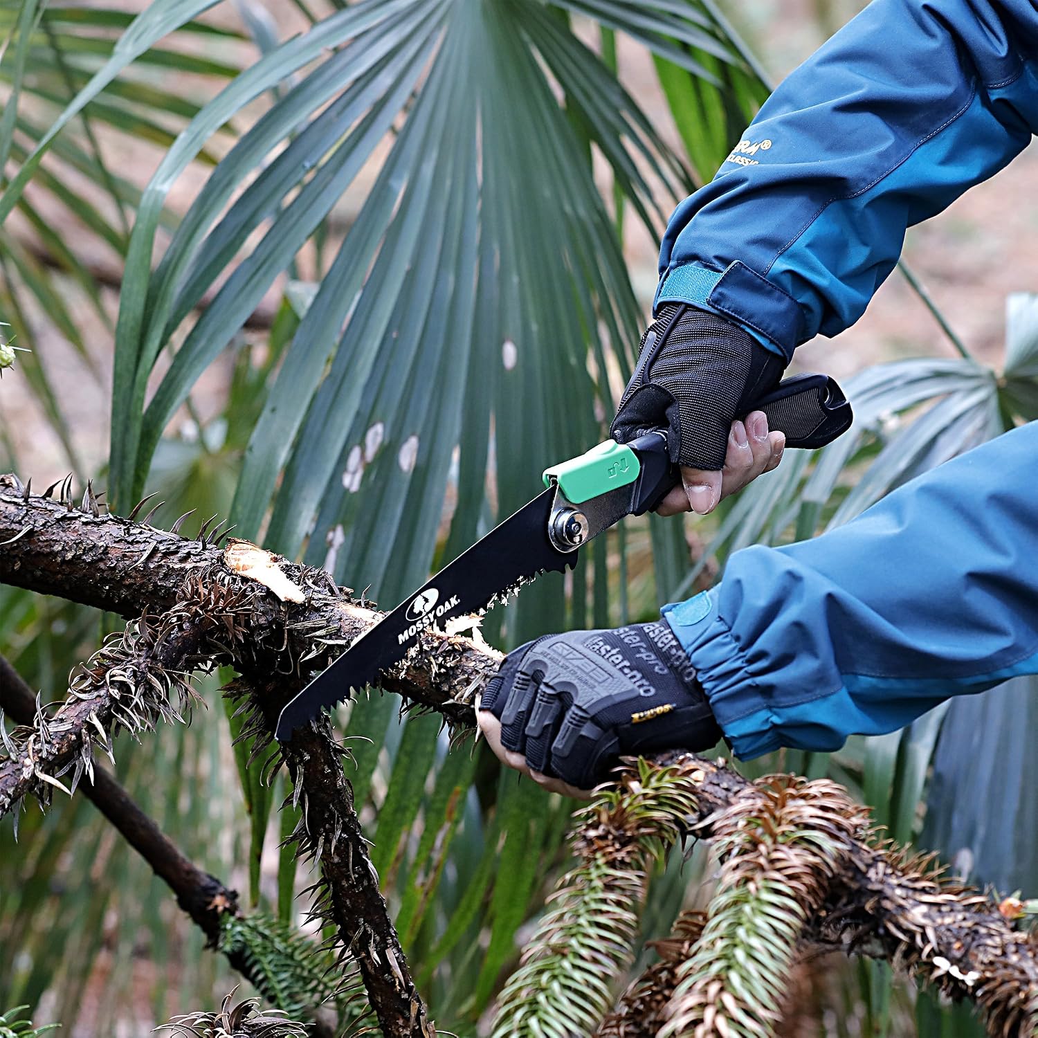 Gloved hands using a Mossy Oak folding saw to cut a branch