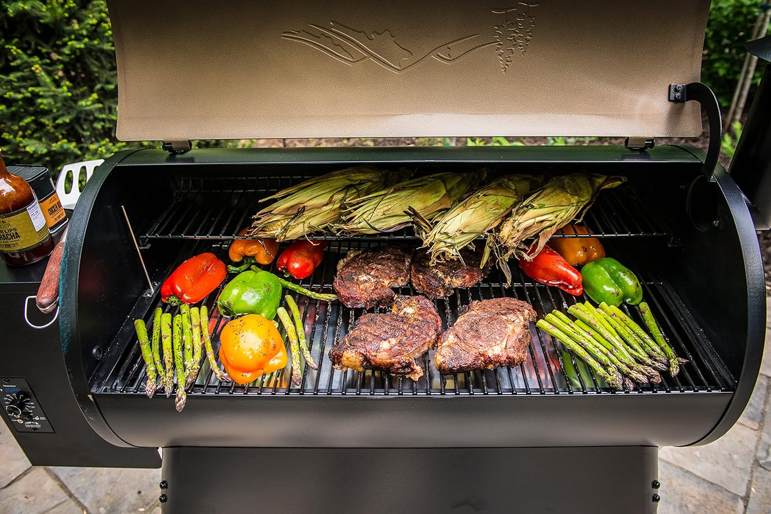 Burgers, corn, and vegetables cooking across a full Traeger pellet grill grate
