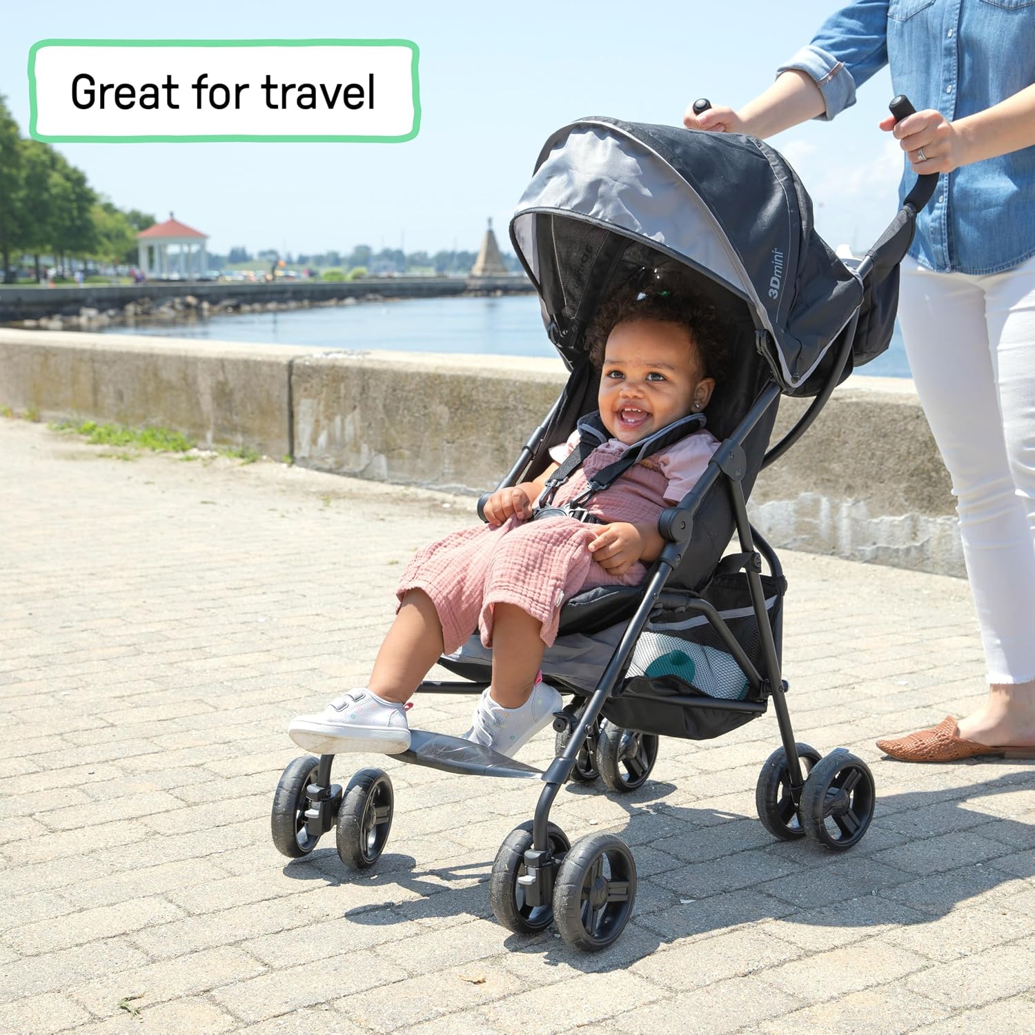 A child smiling in a lightweight Ingenuity 3D Mini stroller on a waterfront walkway